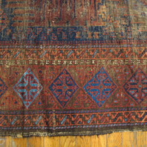 Distressed, low-pile rug in indigo and rust red, featuring large geometric diamond borders on wood planks.