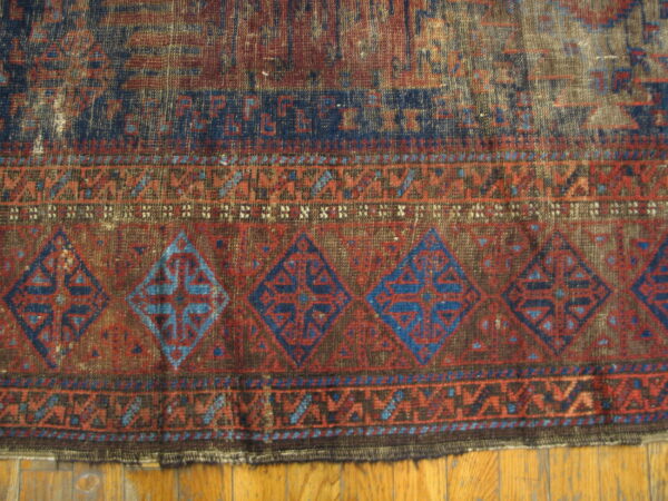 Distressed, low-pile rug in indigo and rust red, featuring large geometric diamond borders on wood planks.