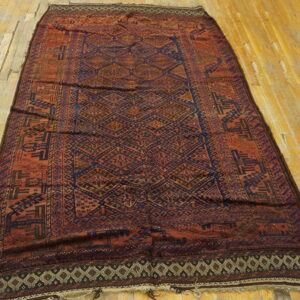 Geometric diamond pattern rug in deep rust and navy blue is laid across light plank wood floors.