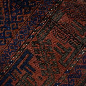 Geometric rug close-up in deep red and navy blue with charcoal details resting on a wood floor.