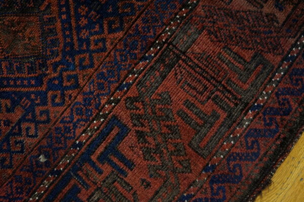 Geometric rug close-up in deep red and navy blue with charcoal details resting on a wood floor.