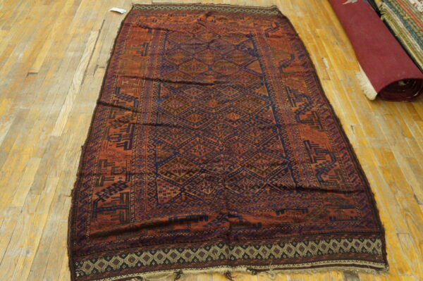 Traditional reddish-brown and dark blue geometric rug with diamond designs lying on a wood floor.