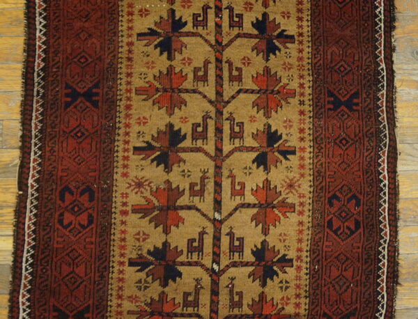 Tan rug with a central tree of life motif and stylized animal figures framed by a reddish-brown geometric border.