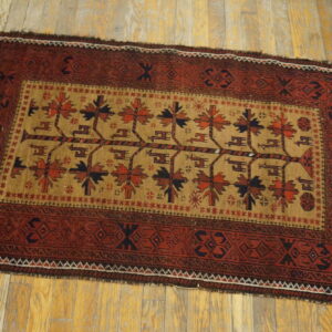 Red and tan rug featuring stylized trees in the field and geometric borders on light wood floors.