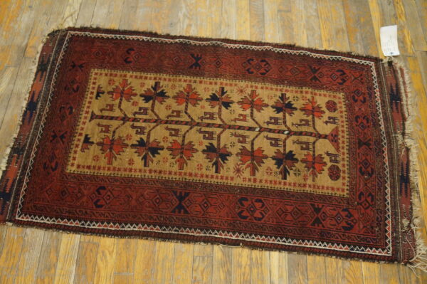 Red and tan rug featuring stylized trees in the field and geometric borders on light wood floors.