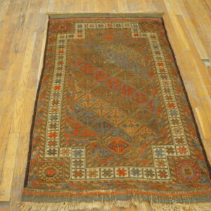 Earth-toned geometric rug with complex medallions in rust and blue rests on worn light plank flooring.