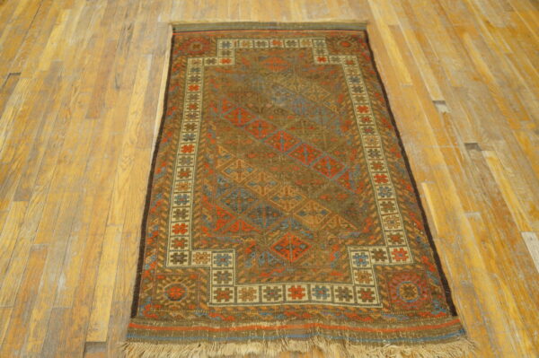 Earth-toned geometric rug with complex medallions in rust and blue rests on worn light plank flooring.