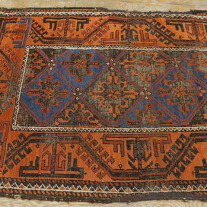 Worn, low-pile rug featuring bold rust-orange and dark blue geometric patterns on light wood.
