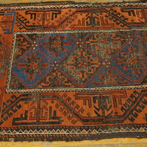 Geometric rug with deep orange and blue diamond patterns lying on light wood floorboards.