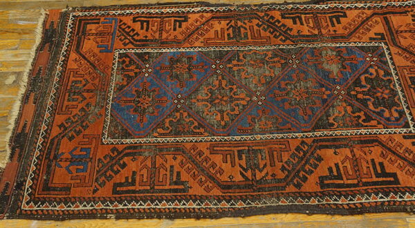 Geometric rug with deep orange and blue diamond patterns lying on light wood floorboards.