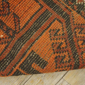 Textured orange and dark brown rug with geometric patterns displayed on weathered light wood flooring.