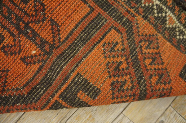 Textured orange and dark brown rug with geometric patterns displayed on weathered light wood flooring.