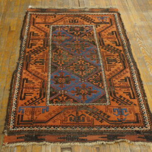 Orange and dark blue geometric rug with a low pile is displayed on worn hardwood planks.