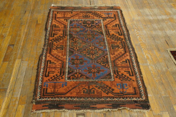 Orange and dark blue geometric rug with a low pile is displayed on worn hardwood planks.