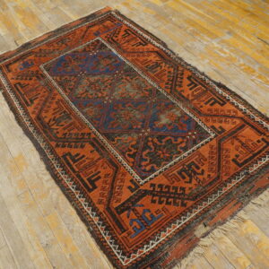 Small tribal rug in orange, black, and blue patterns rests on distressed wooden floorboards.