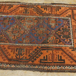 Low-pile rug featuring rusty orange, blue, and black geometric designs on light wood floor planks.