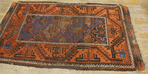 Low-pile rug featuring rusty orange, blue, and black geometric designs on light wood floor planks.