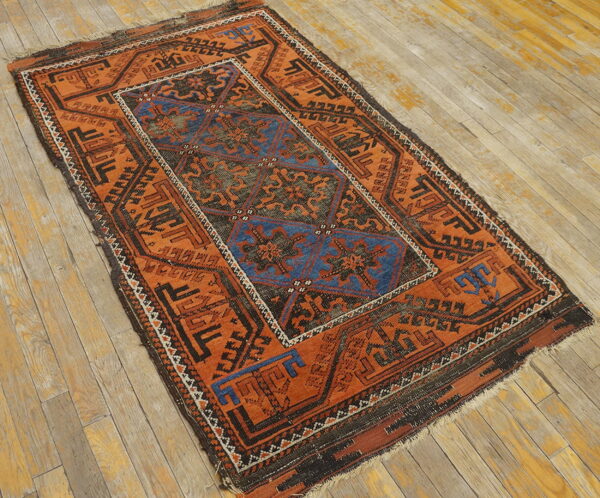 Low-pile orange and blue geometric rug with dark borders on distressed plank flooring.