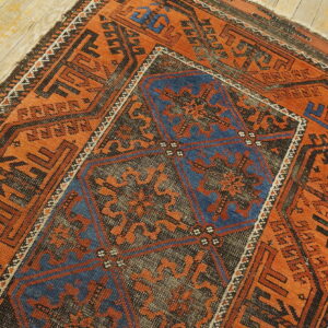 Rust-colored geometric rug with a dark blue center medallion on light wooden floorboards.