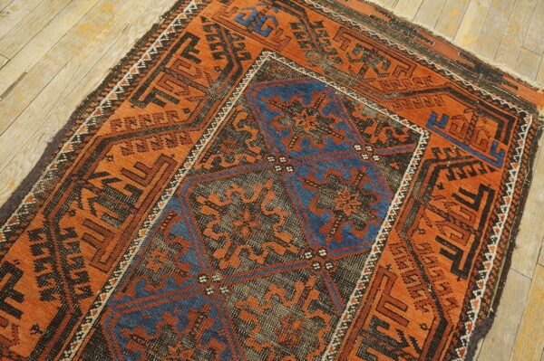 Rust-colored geometric rug with a dark blue center medallion on light wooden floorboards.
