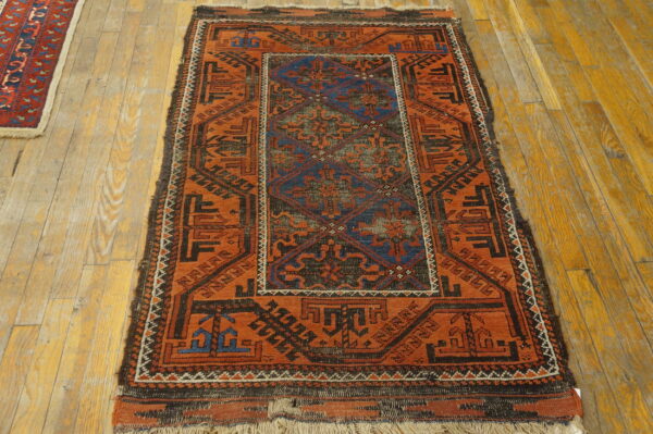 Geometric rug featuring rust orange, black, and blue patterns rests on distressed wooden floorboards.