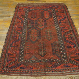 Reddish-orange rug with dark geometric medallions and borders lying on golden wooden floors.