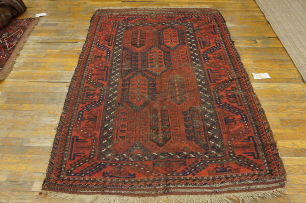 Reddish-orange rug with dark geometric medallions and borders lying on golden wooden floors.