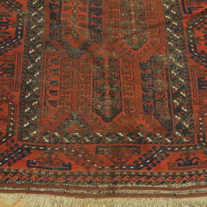Geometric red rug with blue and dark accents, low pile, and fringe resting on wood flooring.