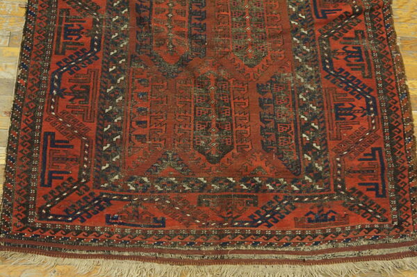 Geometric red rug with blue and dark accents, low pile, and fringe resting on wood flooring.