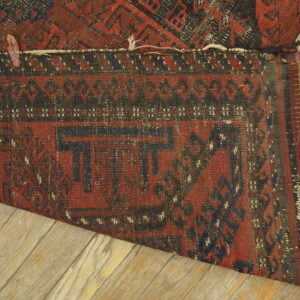 Red and dark patterned rug folded over light wood flooring, revealing tight weaving and fringe.