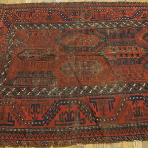 A deep red geometric rug featuring dark blue medallions rests on plank hardwood flooring.