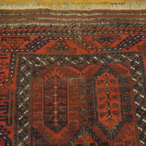 Close-up of a low-pile rug featuring red, dark blue, and brown geometric patterns on wood flooring.
