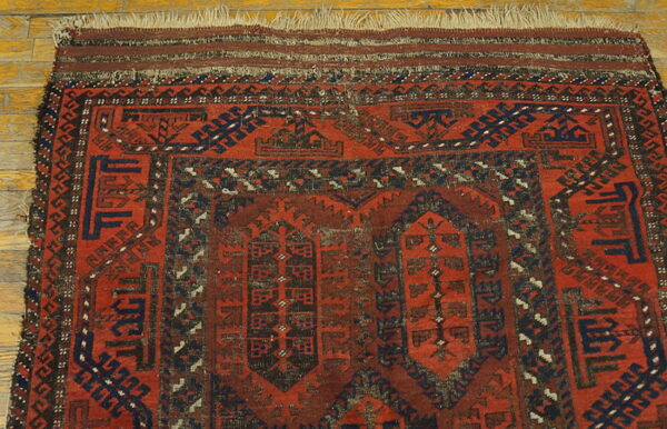 Close-up of a low-pile rug featuring red, dark blue, and brown geometric patterns on wood flooring.