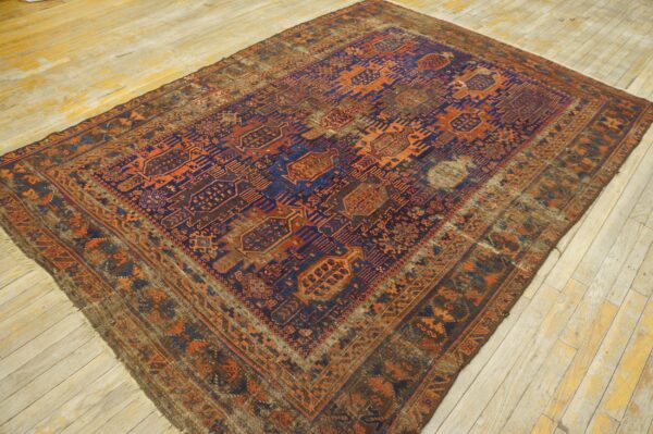 Heavily worn, low-pile rug with geometric blue and orange patterns displayed on yellow wood flooring.