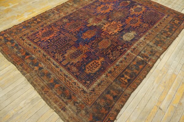 Distressed geometric rug featuring dark blue, rust, and brown colors lying on pale plank wood floor.