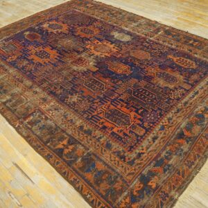 Distressed traditional rug with complex orange and dark blue geometric motifs on wide, pale wood planks.