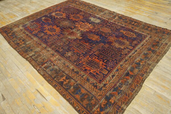 Distressed traditional rug with complex orange and dark blue geometric motifs on wide, pale wood planks.