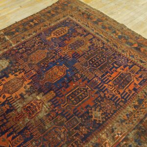 Distressed geometric rug in navy blue, rust orange, and brown tones, covering a portion of light wood flooring.