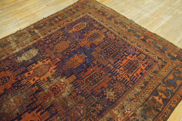 Distressed geometric rug in navy blue, rust orange, and brown tones, covering a portion of light wood flooring.