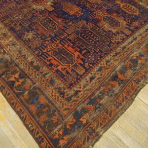 Traditional rug with complex navy and burnt orange geometric patterns lies on light-colored plank wood flooring.