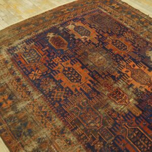 Geometric rug in deep blue and vibrant rust orange with significant fading on distressed wood flooring.