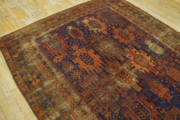 Geometric rug in deep blue and vibrant rust orange with significant fading on distressed wood flooring.