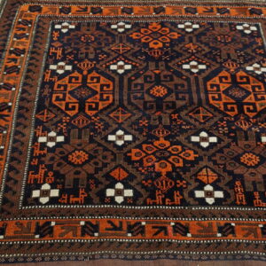 Square tribal rug in navy, orange, and brown geometric motifs, featuring a detailed border, on wood planks.