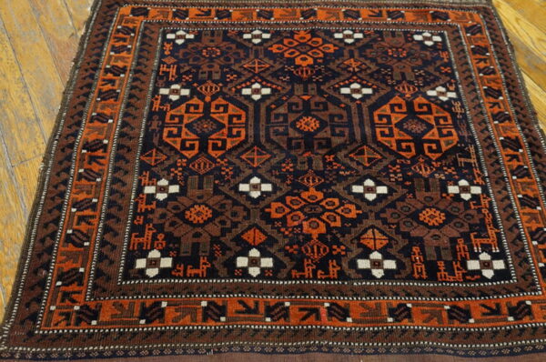 Square tribal rug in navy, orange, and brown geometric motifs, featuring a detailed border, on wood planks.