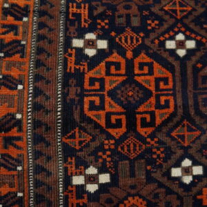 A geometric rust and dark blue tribal rug border and field detail rests on wood flooring.