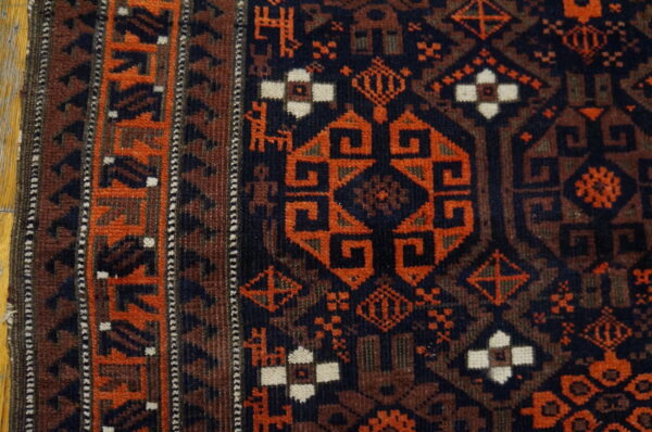 A geometric rust and dark blue tribal rug border and field detail rests on wood flooring.