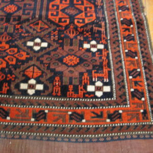 Geometric tribal rug in navy, rust, and orange with stylized figures, resting on light hardwood flooring.