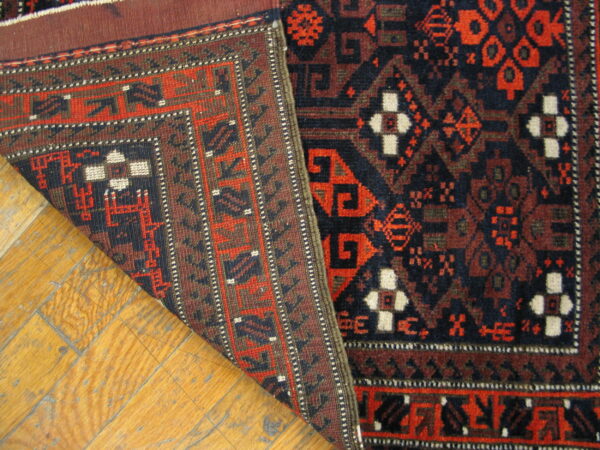 Navy, red, and ivory geometric rug partially folded, showing the woven back on distressed wood plank flooring.