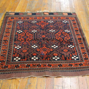 Navy blue and rust orange tribal rug with geometric motifs rests on distressed hardwood flooring.