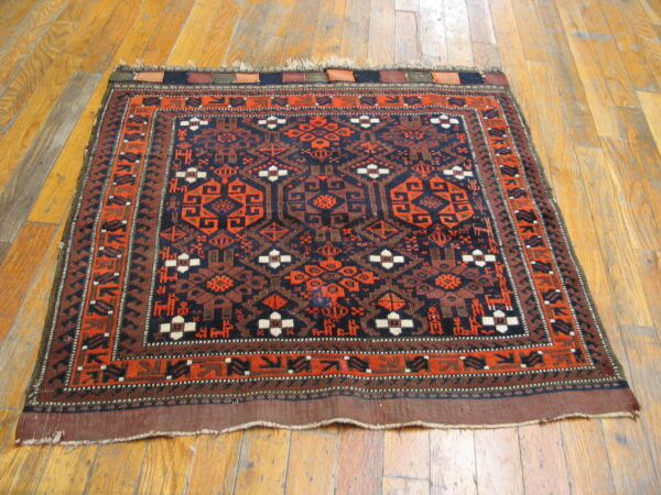 Navy blue and rust orange tribal rug with geometric motifs rests on distressed hardwood flooring.